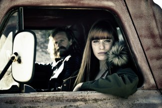 woman and a man sitting in an old pickup, looking into camera