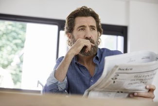 man sitting in the kitchen, reading a newspaper