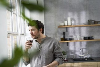 man with coffee standing at the window in his kitchen