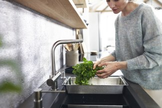 woman cleaning herbs under tap
