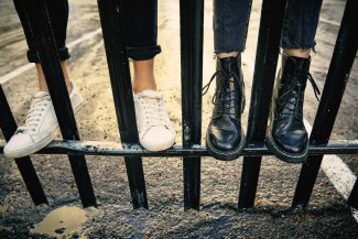 a pair of white and black shoes standing on the lower bar of an iron gate