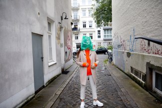 green plastic bag covers face of a young woman, standing on the street