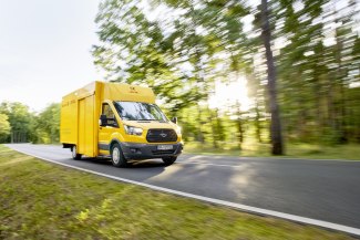 a yellow delivery van driving on the road, with motion blur, in daylight, with green trees in the background,