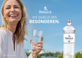 Hier sind Alt-Texte und Hover-Titel für alle vier Anzeigenmotive:  Image 1 (Querformat – Frau outdoor) Alt: A smiling blonde woman holds a sparkling glass of Fürst Bismarck mineral water against a bright blue Hamburg sky, next to a Fürst Bismarck Classic bottle with the tagline "Die Quelle des Besonderen."