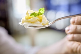 A close-up of a spoon holding a delicate swirl of cream with a fresh basil leaf on top, shot against a soft blurred background.
