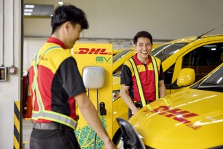 Two DHL employees charge an electric vehicle at a DHL EV charging station.