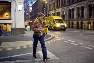 A young woman carrying a DHL parcel crosses a zebra crossing on Tariff Street in Manchester while a yellow DHL van passes in the background