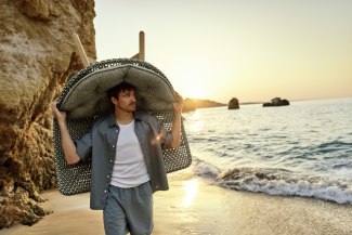 man carrying an big armchair at the beach