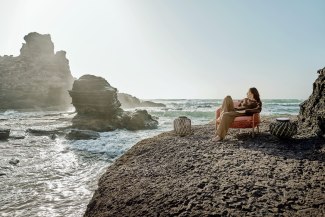 woman in red armchair on cliffs in front of rough sea