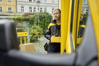 A DHL courier loads parcels from his delivery van on a cobblestone street in front of a Deutsche Post sign