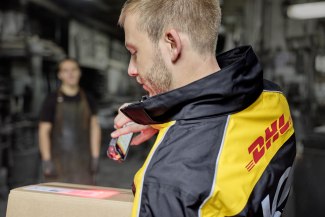 A DHL courier scans a parcel with a handheld device inside a sorting facility. 