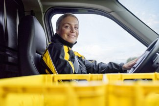 A smiling female Deutsche Post courier sits in the driver's seat of her yellow delivery van ready for her route