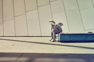 a man in sharkcostume sitting on a bench alone