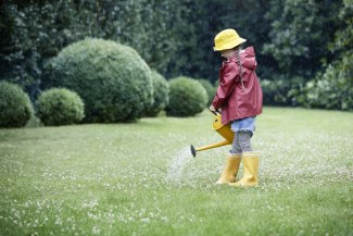 a girl in raincloths is watering a garden lawn