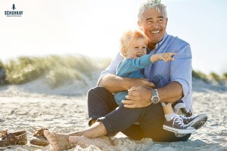 boy sitting on grandfathers lap at the beach