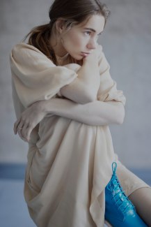 girl in pale skirt sitting in front of concrete wall