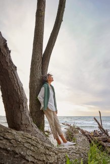 woman standing on treetrunk, looking contemplative into sunset