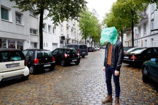 green plastic bag covers face of a young man, standing on the street