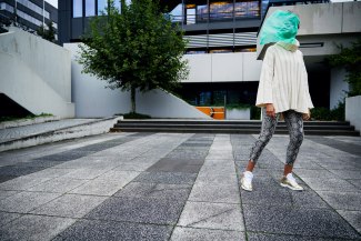 green plastic bag covers face of a young woman, walking between office buildings