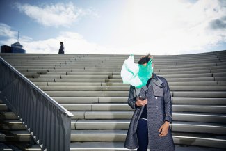 green plastic bag covers face of a young man, checking the display of his mobilephone