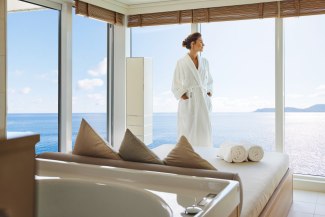 young woman a leaning against a window in a spa, looking towards an ocean landscape