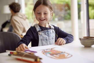 young girl at table, laughing while chosing a pencil young girl at table, laughing while chosing a pencil